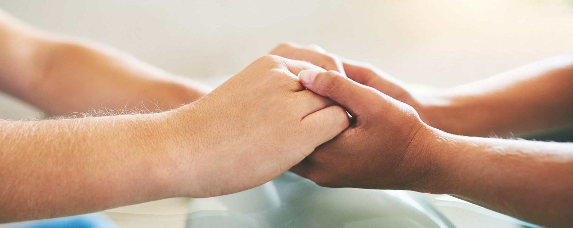An adult's hand gently holding a premature baby's hand